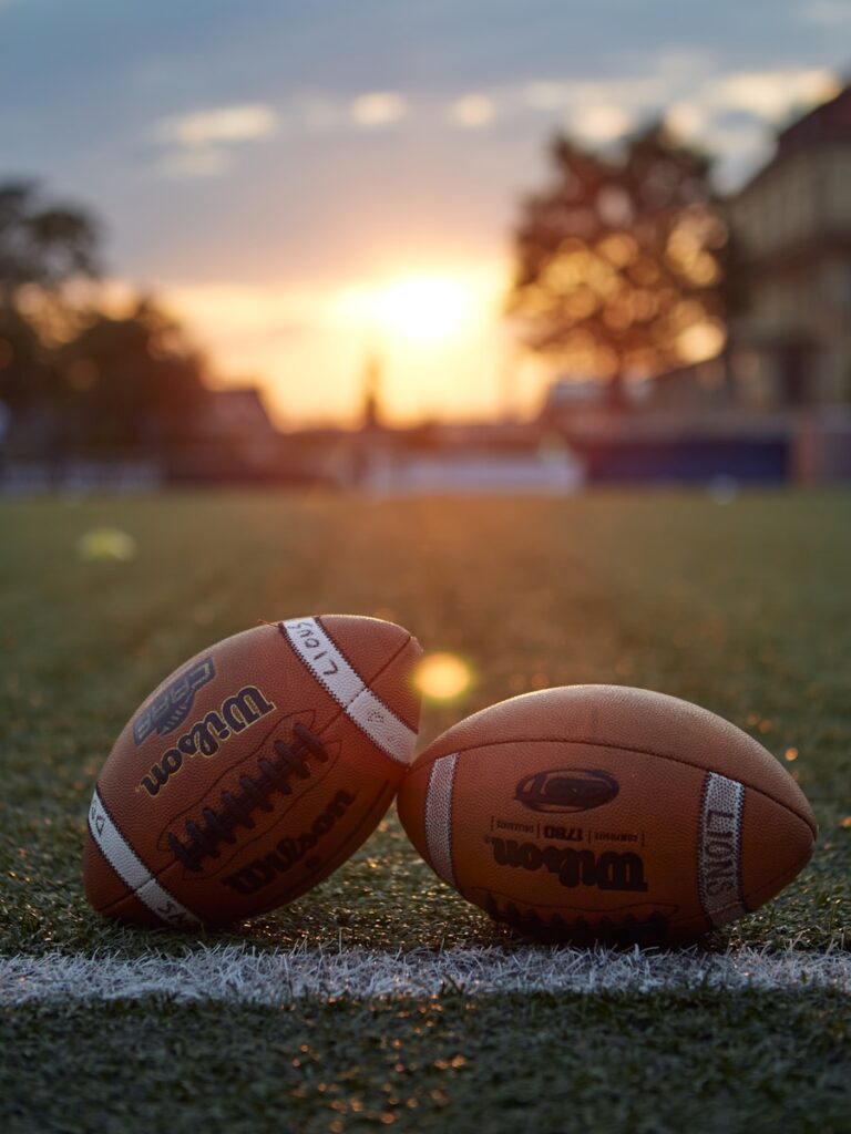 Two footballs sitting on a football field at sunset